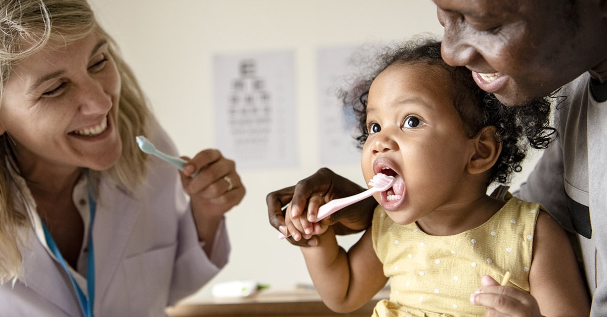 parent and doctor showing young child how to brush teeth